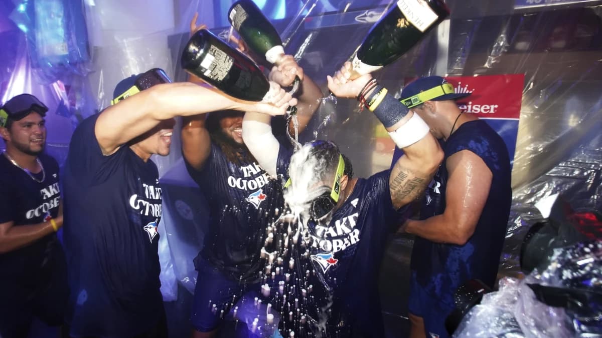 Toronto Blue Jays pitcher Jose Berrios (left) and first baseman Vladimir Guerrero Jr. (centre) pour champagne on third baseman Santiago Espinal (5) after clinching a wild card berth after a series against the Tampa Bay Rays at Roge