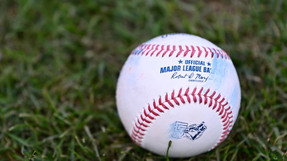 An official MLB baseball with a Toronto Blue Jays logo sits on the grass before a game against the Boston Red Sox at Fenway Park.